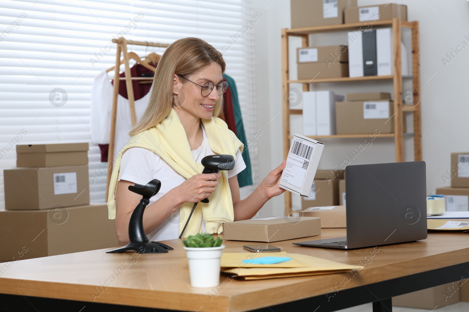 Photo of Seller with scanner reading parcel barcode in office. Online store