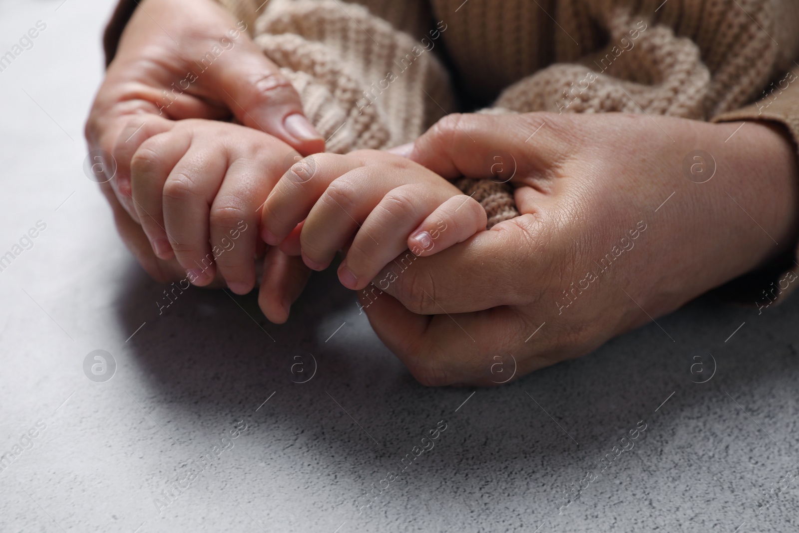 Photo of Woman holding hands with her little daughter at light grey table, closeup