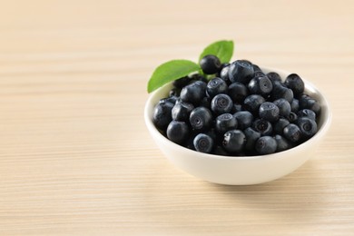 Photo of Tasty fresh bilberries with leaves in bowl on light table. Space for text