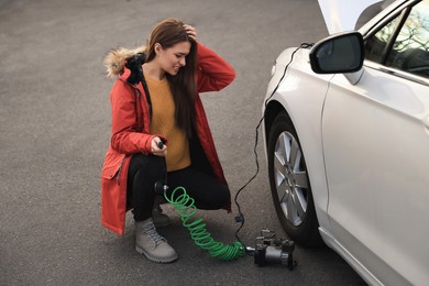 Photo of Young woman trying to inflate car tire with air compressor on street