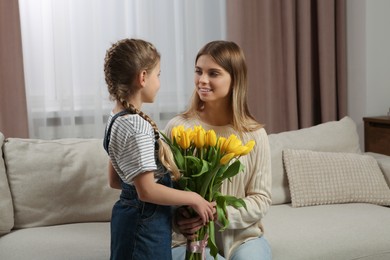 Photo of Little daughter congratulating mom with bouquet of yellow tulips at home. Happy Mother's Day
