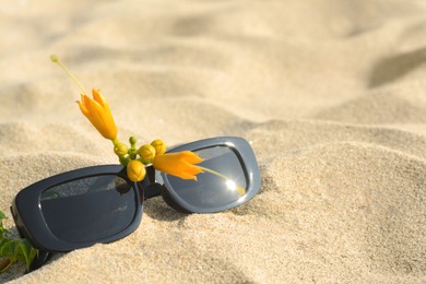Photo of Stylish sunglasses and tropical flower on sand, closeup. Space for text