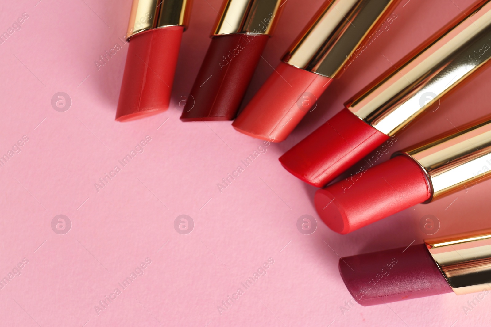Photo of Set of bright lipsticks in gold tubes on pink background, flat lay. Space for text