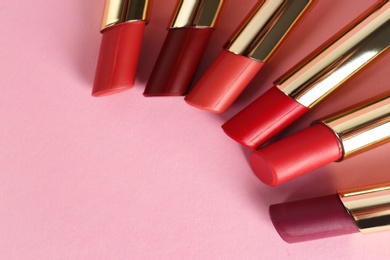 Set of bright lipsticks in gold tubes on pink background, flat lay. Space for text