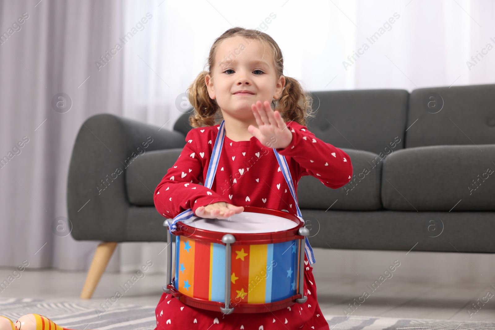 Photo of Little girl playing toy drum at home