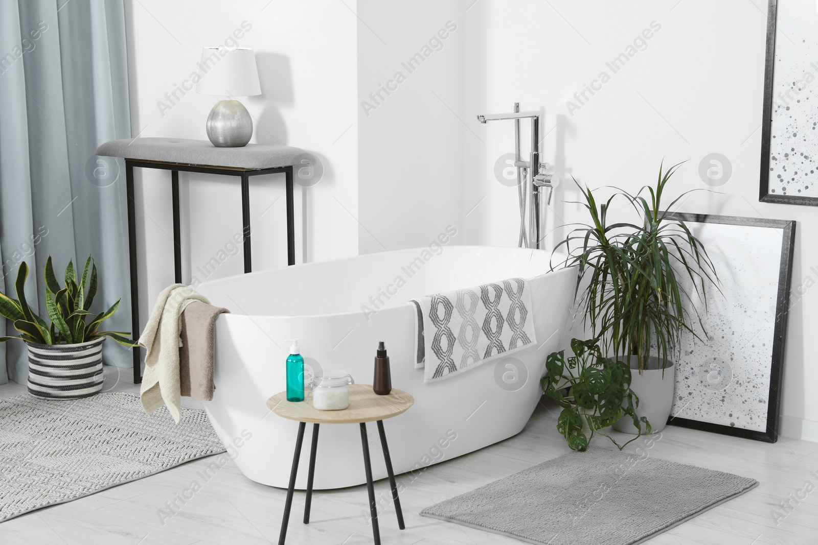 Photo of Stylish white tub and wooden table with toiletries in bathroom. Interior design