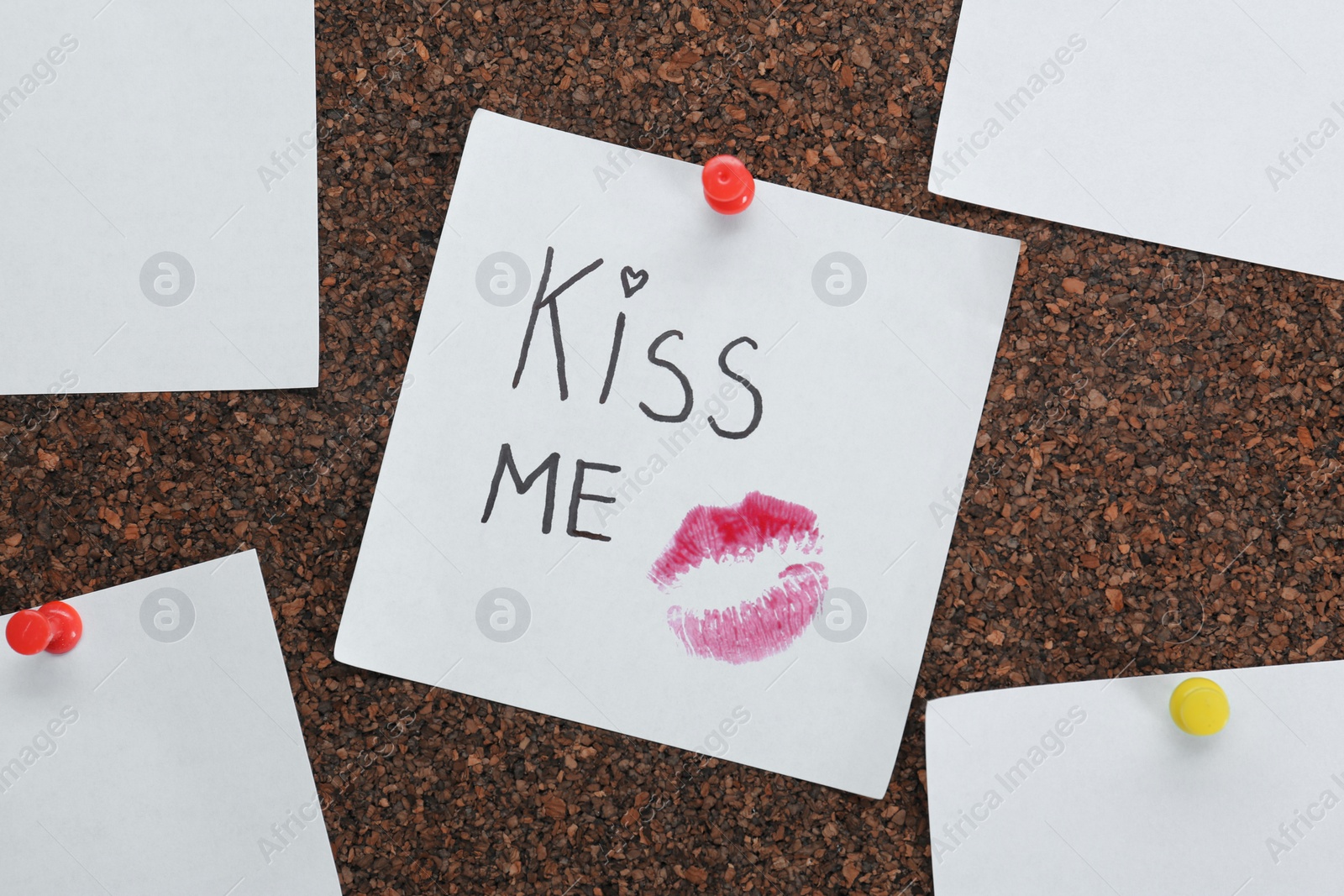 Note with lipstick mark and phrase Kiss Me on cork board Photo of Note with lipstick mark and phrase Kiss Me on cork board