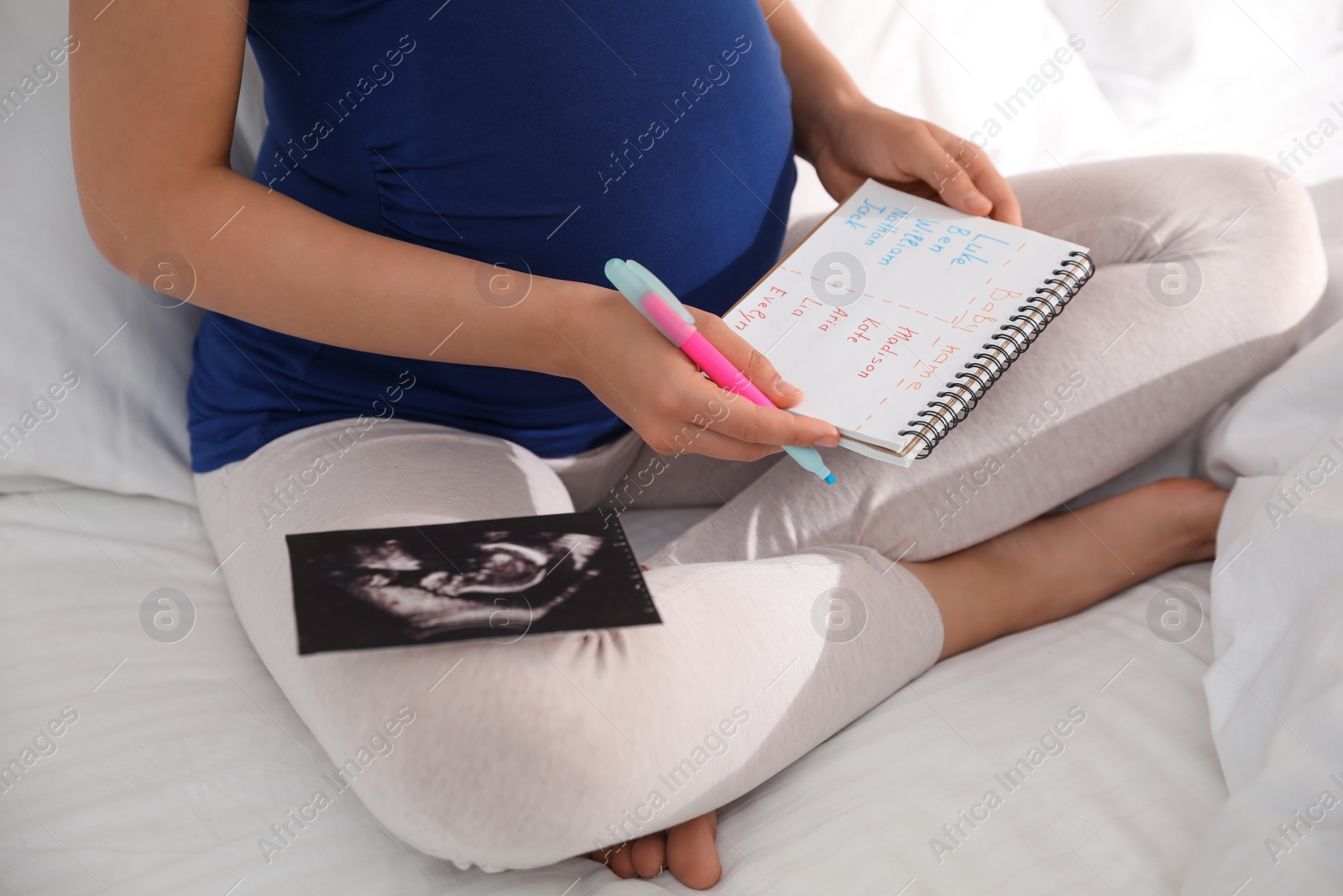 Photo of Pregnant woman with baby names list and sonogram sitting on bed, closeup