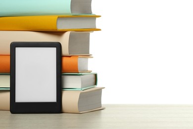 Stack of hardcover books and modern e-book on wooden table against white background. Space for text