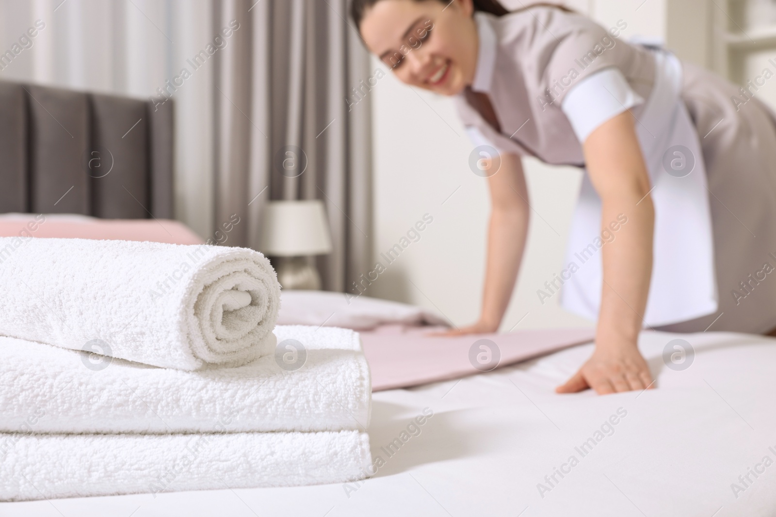 Photo of Young maid making bed in hotel room, selective focus