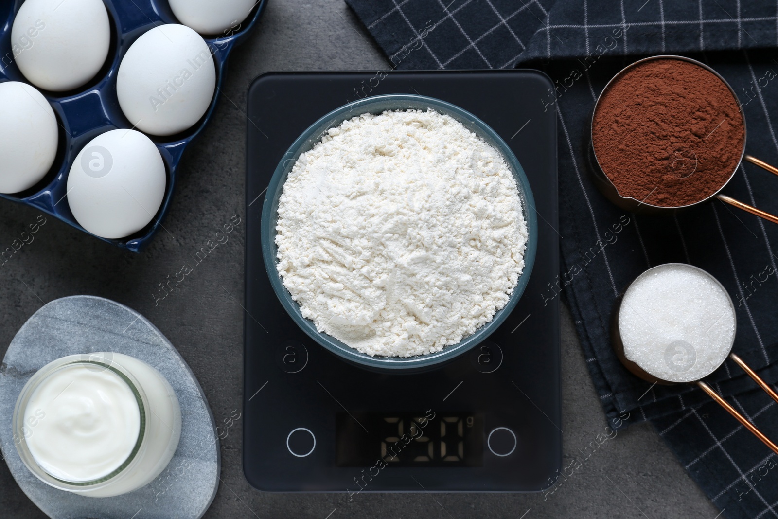 Photo of Electronic scales with flour and different products on black table, flat lay