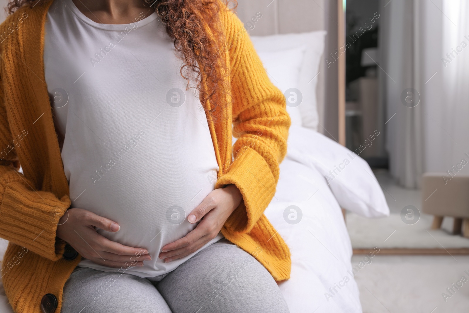 Photo of Pregnant African-American woman sitting on bed at home, closeup