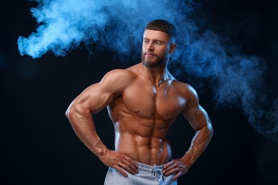 Young bodybuilder with muscular body in smoke on color background
