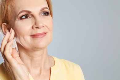 Portrait of mature woman with beautiful face on grey background. Space for text