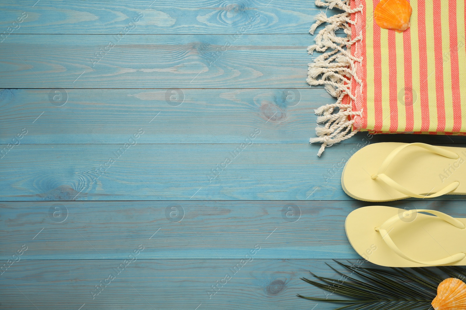 Photo of Beach towel and flip flops on light blue wooden background, flat lay. Space for text