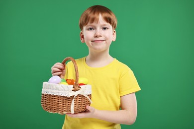 Easter celebration. Cute little boy with wicker basket full of painted eggs on green background