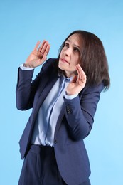 Woman in suit avoiding something on light blue background