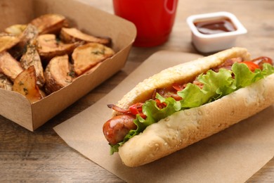 Photo of Hot dog, potato wedges and ketchup on wooden table, closeup. Fast food
