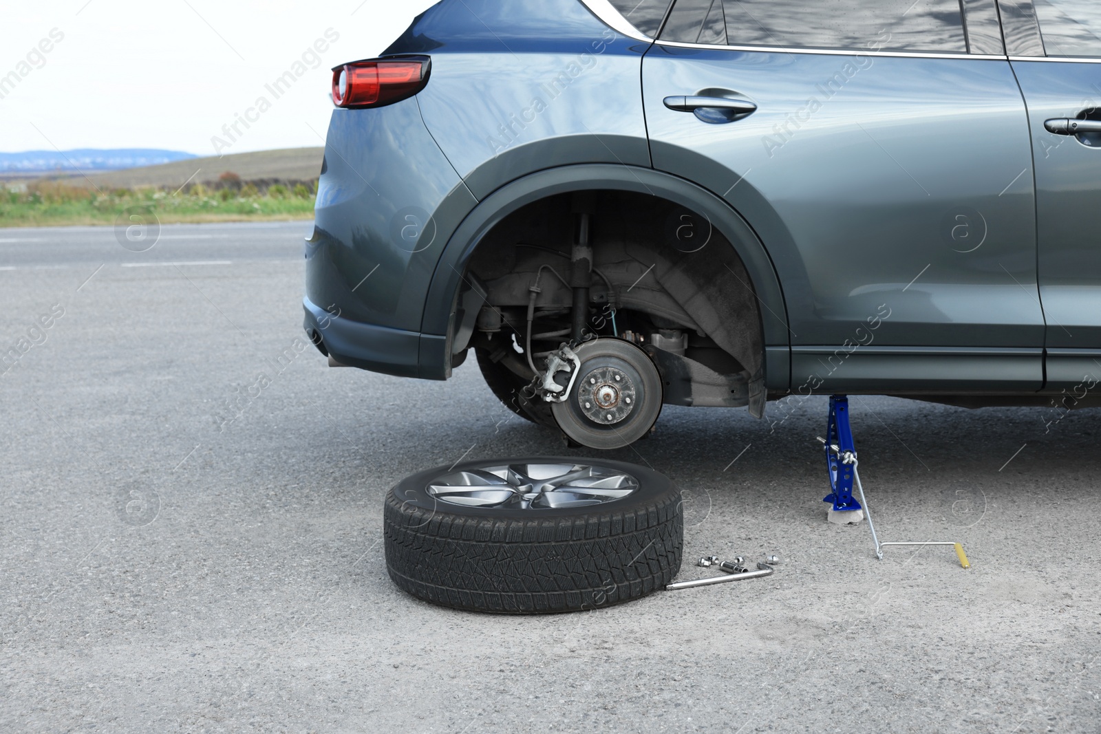 Photo of Car lifted by scissor jack and new wheel on roadside outdoors. Tire puncture