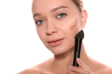 Young woman applying foundation on her face against white background