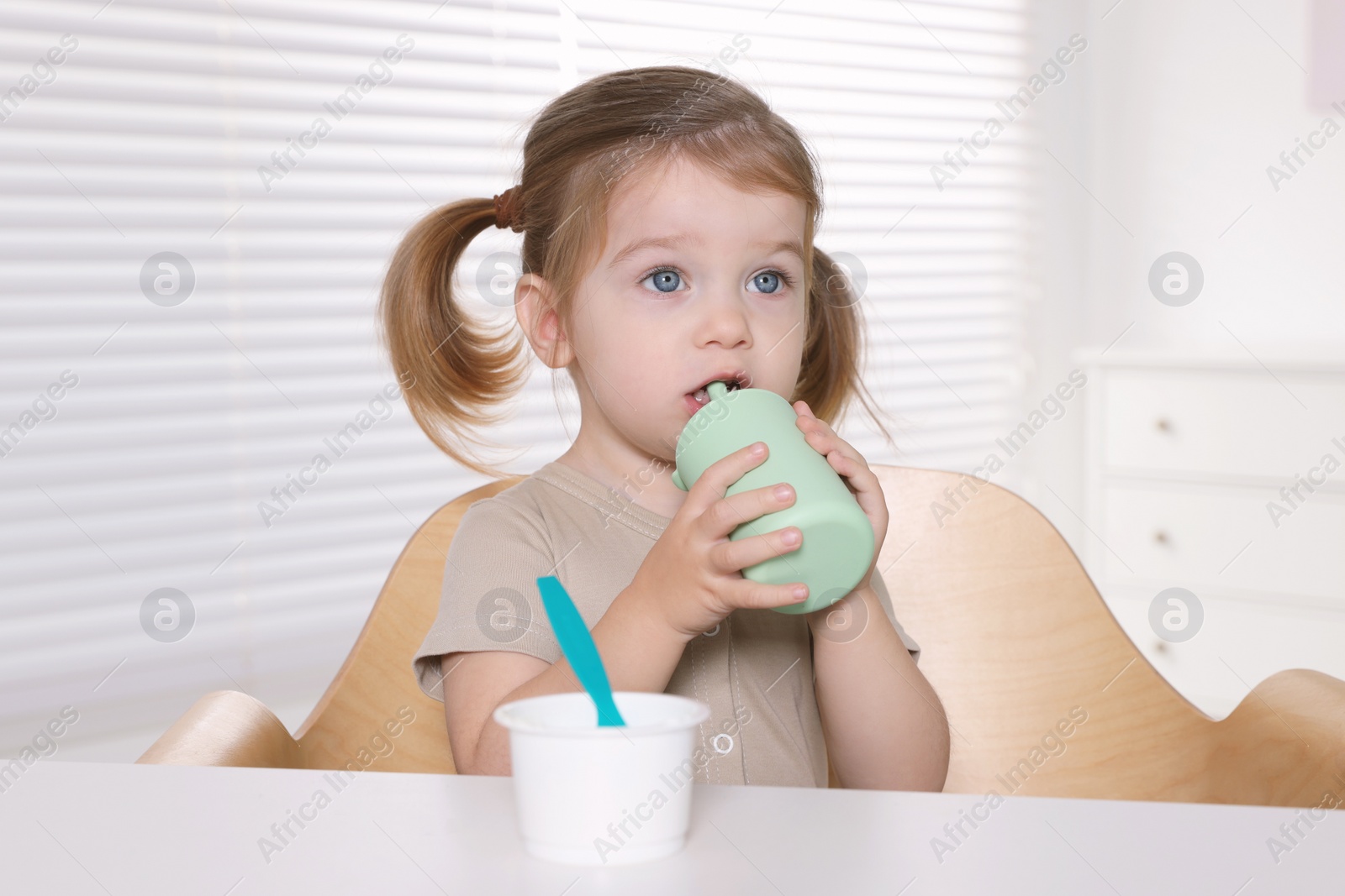 Photo of Cute little child with bottle and cup of tasty yogurt at white table indoors