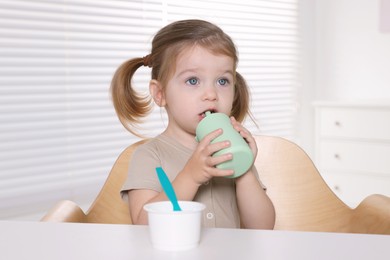 Photo of Cute little child with bottle and cup of tasty yogurt at white table indoors