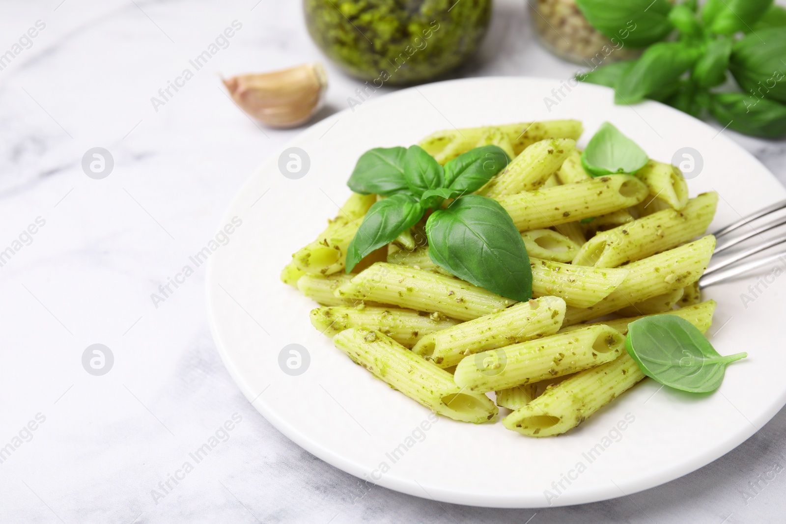 Photo of Delicious pasta with pesto sauce and basil on white marble table, closeup. Space for text