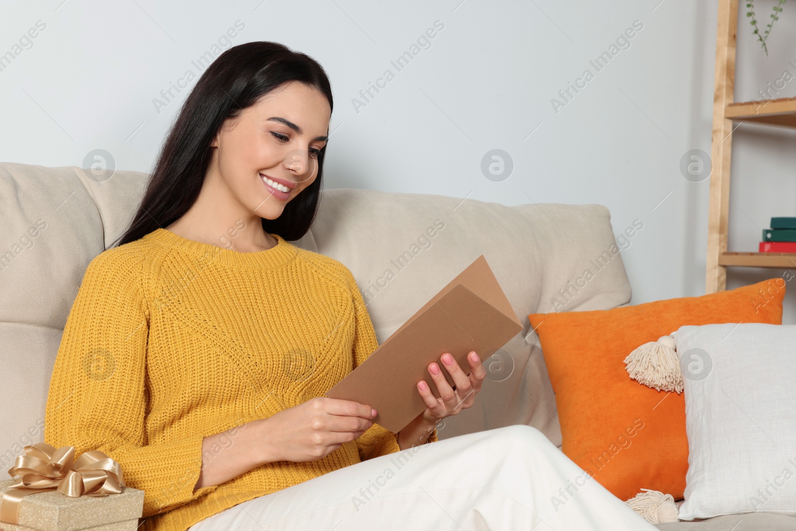 Photo of Happy woman reading greeting card on sofa in living room