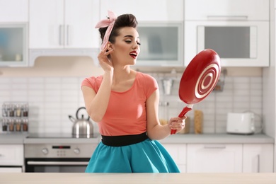 Photo of Funny young housewife with frying pan in kitchen