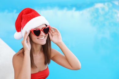 Young woman wearing Santa Claus hat near swimming pool. Christmas vacation