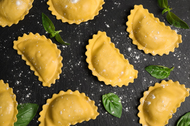 Raw ravioli with basil on black table, flat lay. Italian pasta