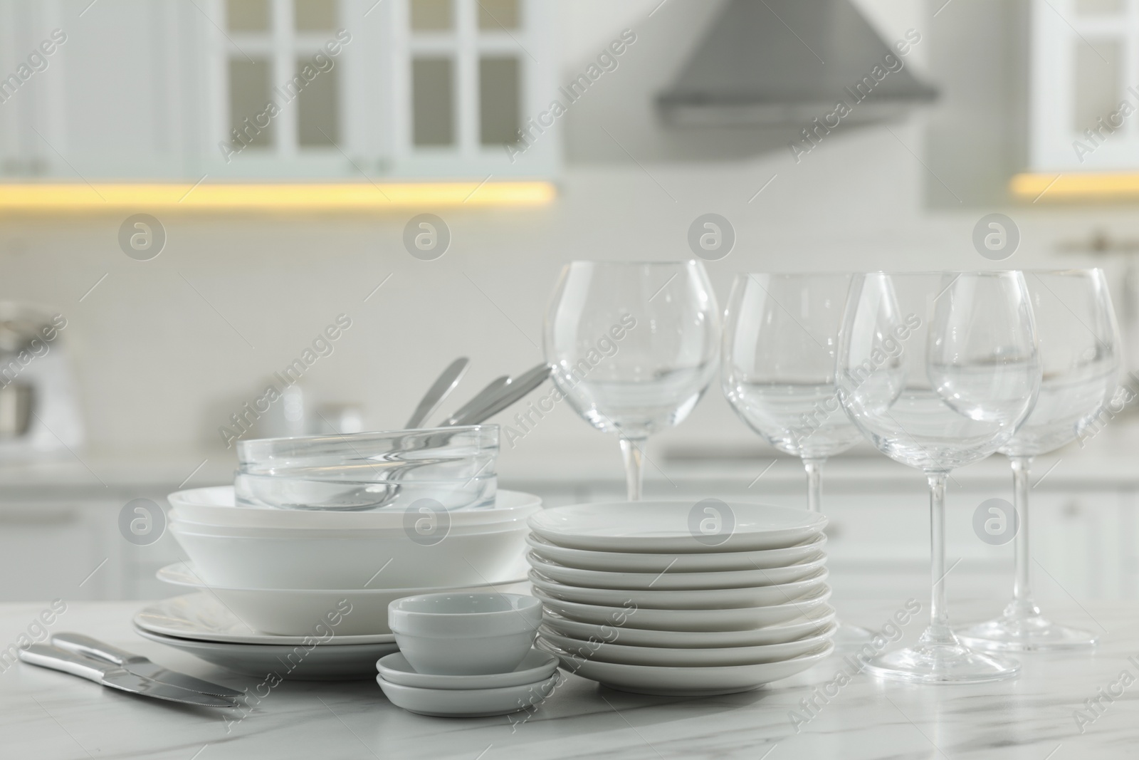 Photo of Different clean dishware, cutlery and glasses on white marble table in kitchen