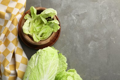 Photo of Fresh ripe Chinese cabbages and green leaves in bowl on gray textured table, flat lay. Space for text