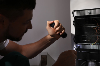 Electrician with flashlight fixing refrigerator indoors, closeup