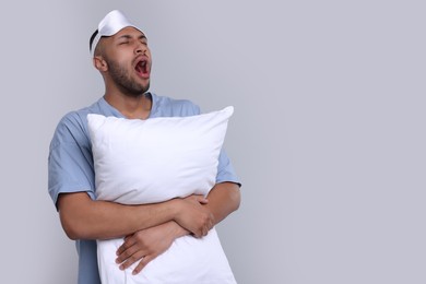 Photo of Man with pillow and sleep mask yawning on light grey background, space for text. Insomnia problem