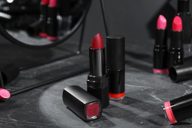 Photo of Different beautiful lipsticks and mirror on grey marble table, closeup