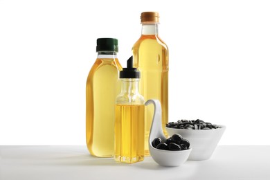 Photo of Bottles of different cooking oils, olives and sunflower seeds on white background