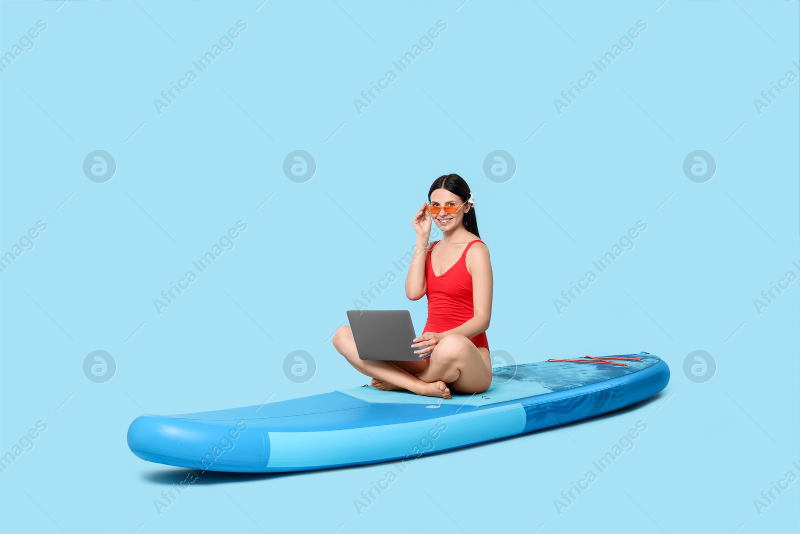 Photo of Happy woman with laptop on SUP board against light blue background