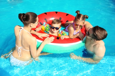 Photo of Young family with little children in swimming pool on sunny day