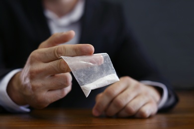 Photo of Criminal holding drug at table indoors, closeup