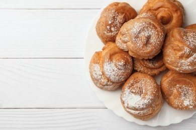 Photo of Delicious profiteroles with powdered sugar on white wooden table, top view. Space for text