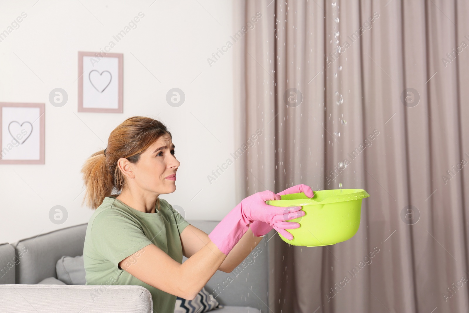 Photo of Woman collecting leaking water from ceiling in living room. Time to call plumber