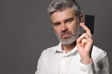 Handsome man holding blank business card on grey background. Space for text