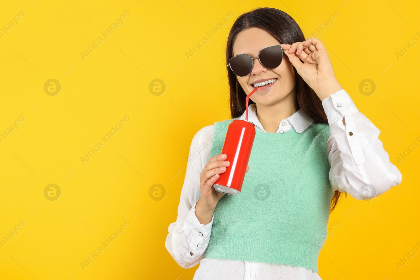 Photo of Beautiful happy woman drinking from red beverage can on yellow background. Space for text