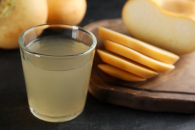 Glass of fresh natural turnip juice, cut and whole roots on black table, closeup. Space for text