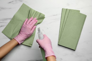 Photo of Woman in gloves cleaning light table with paper towel and detergent, top view