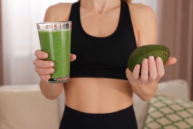 Photo of Young woman in sportswear with glass of fresh smoothie and avocado at home, closeup