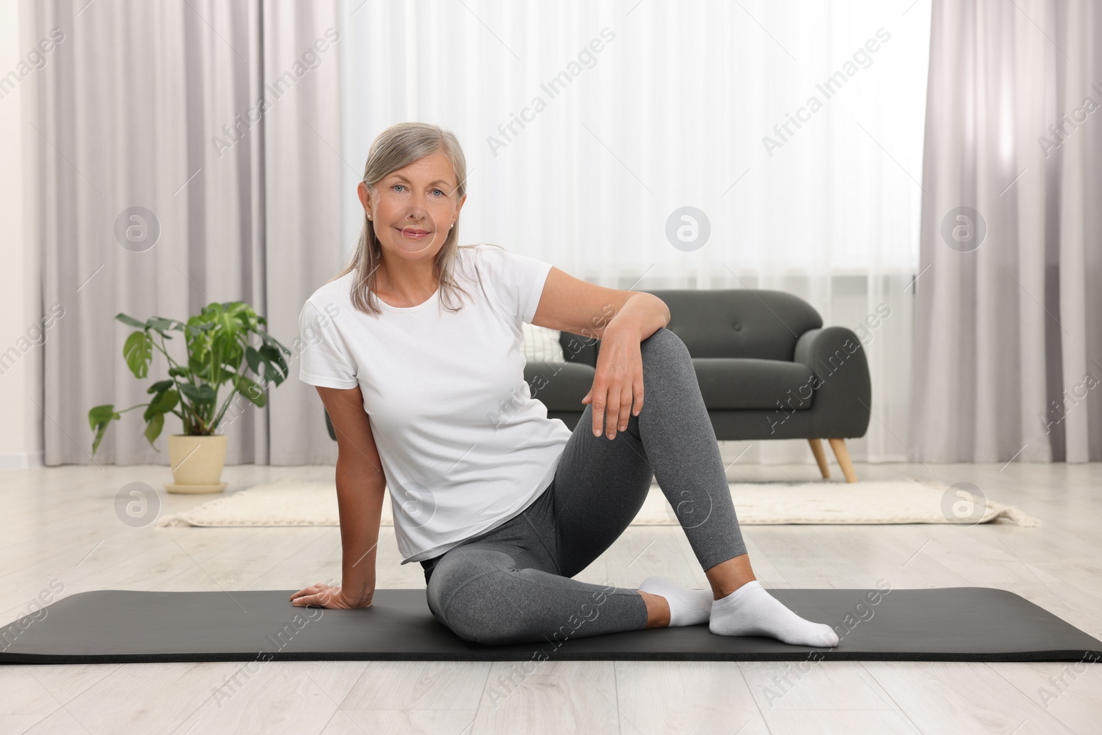 Photo of Happy senior woman sitting on mat at home. Yoga practice