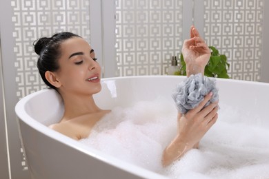 Woman taking bath with mesh pouf indoors