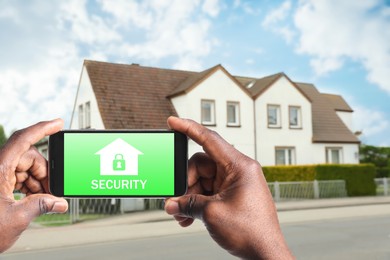 Image of Home security system. African American man with smartphone near his house outdoors, closeup